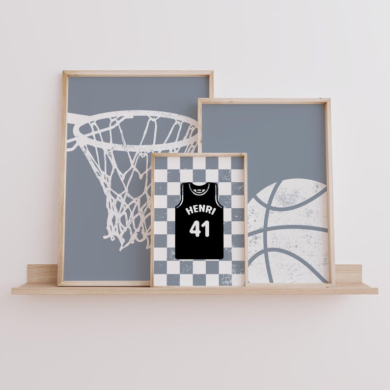 May include: Three framed prints on a wooden shelf. The prints feature a basketball hoop, a basketball jersey with the name "HENRI" and the number "41", and a basketball. The background of the prints is a light grey colour.