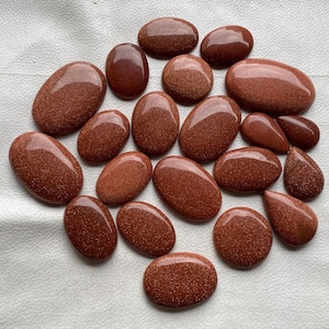 May include: A collection of 20 smooth, oval-shaped, red-brown sandstone cabochons. The stones are polished and have a natural, earthy look.