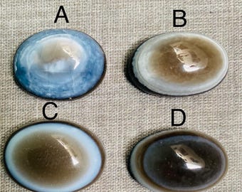 May include: Four oval cabochons with polished surfaces. Each has a unique colour pattern: blue, brown, brown with white, and dark brown. The cabochons are labelled A, B, C, and D.
