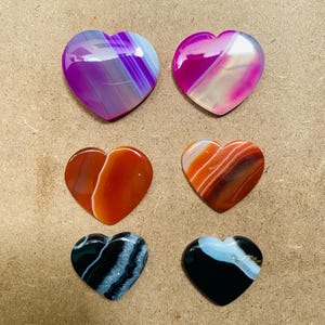 May include: Six heart-shaped agate stones with different color patterns. The stones are polished and have a smooth, glossy finish. The colors include pink, purple, orange, and black.