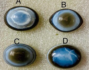 May include: Four oval cabochons with a dark border. The cabochons feature a blue and white swirling pattern, with variations in the centre. One has a star-like pattern. Suitable for jewellery making or other crafts.