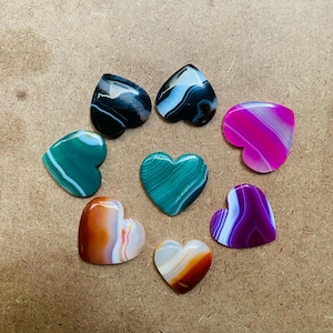 May include: Seven heart-shaped agate stones in various colors, including green, pink, purple, black, and white. The stones are polished and have a smooth, shiny surface.