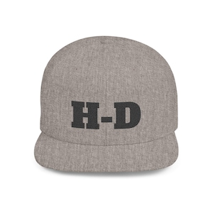 Puede incluir: Gorra de béisbol gris con visera plana. La gorra presenta las letras negras "H-D" centradas en la parte delantera. El sombrero está hecho de una tela texturizada.
