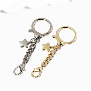 May include: Two keychains with star charms. One keychain is silver with a silver star charm and the other is gold with a gold star charm.