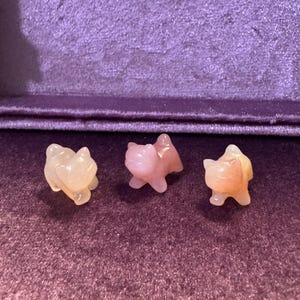 Puede incluir: Tres pequeñas figuritas de gato talladas en cuarzo rosa.