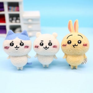 Puede incluir: Tres pequeñas figuritas de animales de fieltro. Un gato blanco con orejas azules, un oso blanco y un conejo amarillo. Cada figurita tiene una cara linda de estilo de dibujos animados con ojos negros y un pequeño rubor rosado.