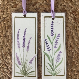 Puede incluir: Dos marcapáginas con temática de lavanda con flores moradas y hojas verdes. Los marcapáginas están enmarcados con un borde dorado y tienen una cinta morada.