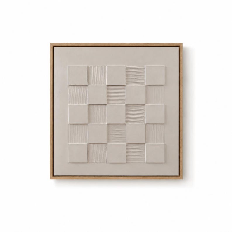 Pu&ograve; includere: Un'opera d'arte murale quadrata con un motivo a scacchiera testurizzato color beige chiaro all'interno di una cornice in legno naturale. Il design &egrave; composto da quadrati lisci in rilievo alternati a quadrati con sottili linee verticali.