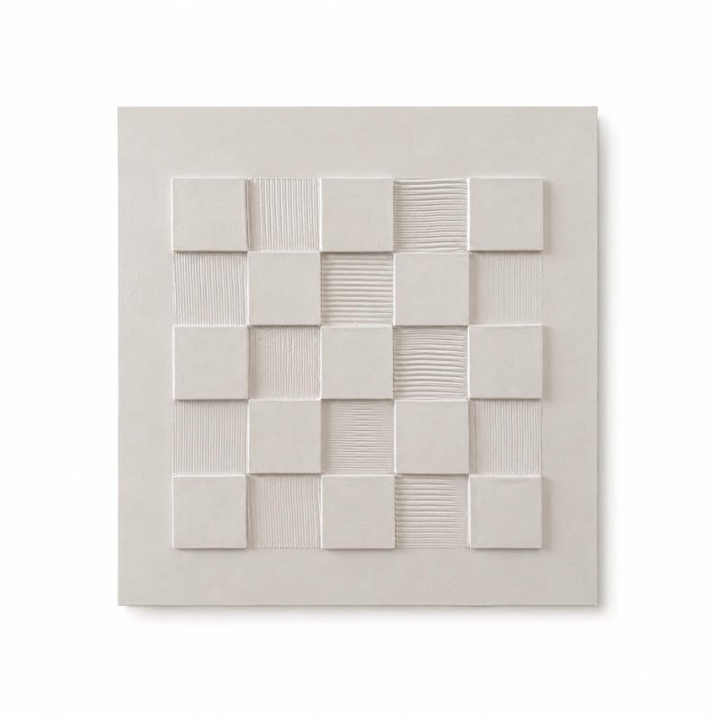 Pu&ograve; includere: Un pannello da parete quadrato color bianco sporco caratterizzato da un motivo a scacchiera in rilievo. Il design alterna quadrati a superficie liscia e piatta a quadrati con texture a linee sottili, verticali o orizzontali, creando un effetto a griglia.