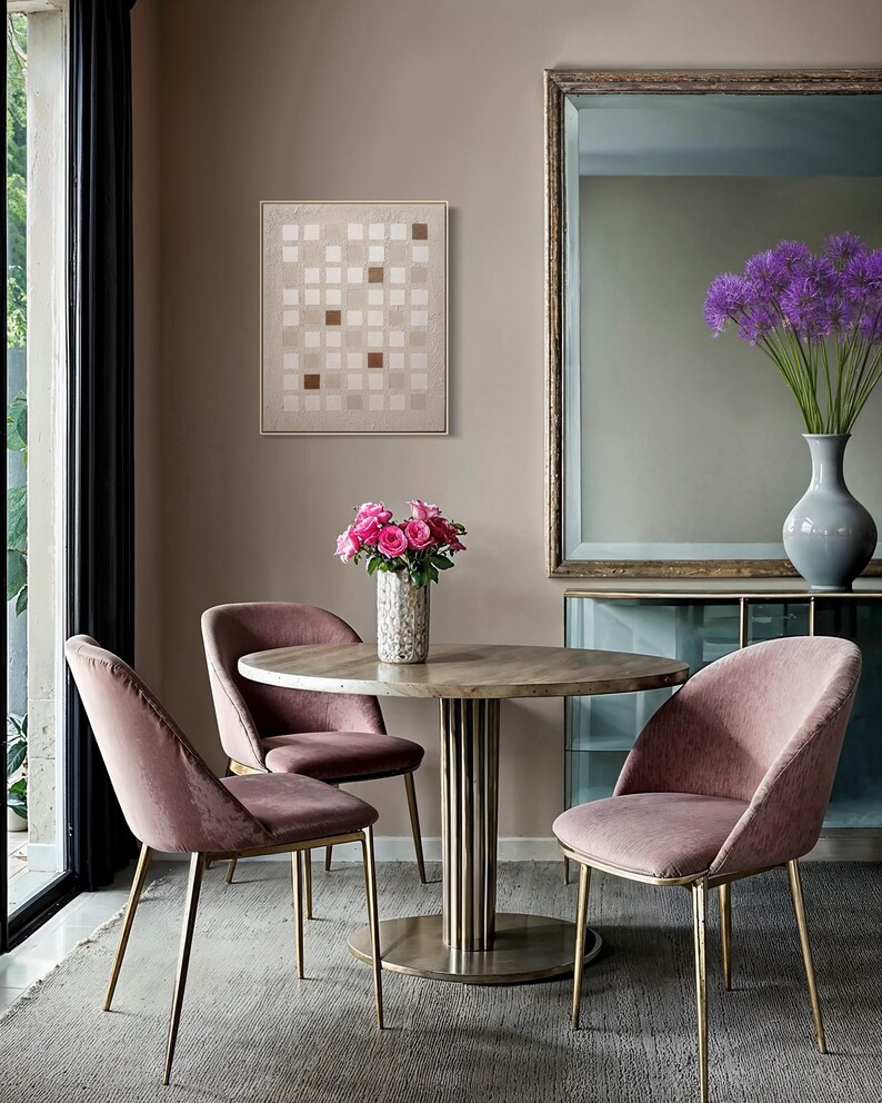 K&ouml;nnte beinhalten: Ein Esszimmer mit einem runden Tisch auf einem Messingfu&szlig;, umgeben von drei rosa Samtst&uuml;hlen mit goldenen Beinen. Eine Vase mit rosa Rosen schm&uuml;ckt den Tisch. Ein abstraktes Kunstwerk h&auml;ngt an der Wand und ein gro&szlig;er Spiegel ist sichtbar.