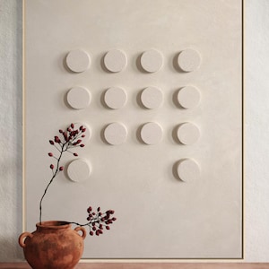 Peut inclure: Un vase en terre cuite contenant des baies rouges est plac&eacute; devant un mur textur&eacute; blanc cass&eacute; avec une grille d'&eacute;l&eacute;ments circulaires en relief. L'&oelig;uvre est encadr&eacute;e d'une fine bordure dor&eacute;e, cr&eacute;ant une esth&eacute;tique minimaliste et terreuse.