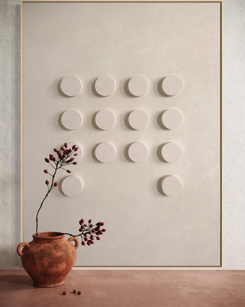 Peut inclure: Un vase en terre cuite contenant des baies rouges est plac&eacute; devant un mur textur&eacute; blanc cass&eacute; avec une grille d'&eacute;l&eacute;ments circulaires en relief. L'&oelig;uvre est encadr&eacute;e d'une fine bordure dor&eacute;e, cr&eacute;ant une esth&eacute;tique minimaliste et terreuse.