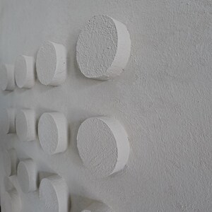 Peut inclure: Une &oelig;uvre d'art murale textur&eacute;e blanc cass&eacute; avec une s&eacute;rie de formes cylindriques en relief. Les cylindres sont espac&eacute;s uniform&eacute;ment, cr&eacute;ant un effet tridimensionnel. L'&oelig;uvre a une esth&eacute;tique minimaliste.