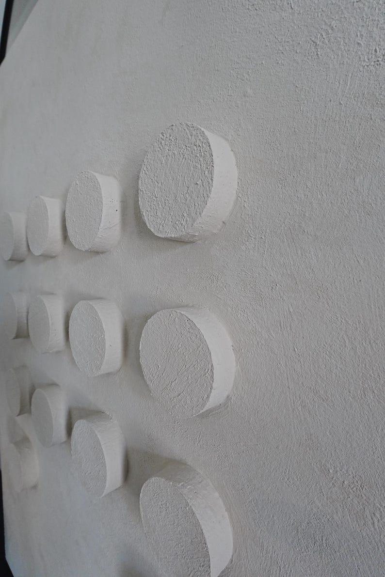 Peut inclure: Une &oelig;uvre d'art murale textur&eacute;e blanc cass&eacute; avec une s&eacute;rie de formes cylindriques en relief. Les cylindres sont espac&eacute;s uniform&eacute;ment, cr&eacute;ant un effet tridimensionnel. L'&oelig;uvre a une esth&eacute;tique minimaliste.