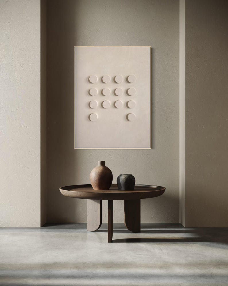 May include: A modern interior scene featuring a beige wall art piece with a grid of circular indentations. Below, a dark wooden, round coffee table with two ceramic vases in brown and black. The room has a neutral color palette.