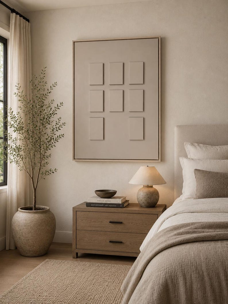 May include: A framed wall art piece featuring a light beige surface with eight raised rectangular panels arranged in a grid. The artwork is displayed above a wooden nightstand with two drawers, a small lamp, and stacked books in a bedroom setting.