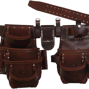 May include: A brown leather tool belt with multiple pouches and pockets. The belt has a buckle closure and a separate leather strap. Rivets secure the pockets and belt components. The tool belt is designed for construction or carpentry work.