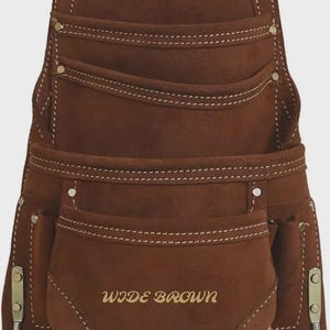 Może przedstawiać: Brązowy skórzany pas narzędziowy z wieloma kieszeniami i metalową pętlą do zawieszania. Pas posiada białe przeszycia, a z przodu widnieje napis "WIDE BROWN". Posiada metalowe okucia.