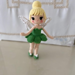 May include: A crocheted fairy doll with blonde hair, a green dress, and white wings. The doll has a sweet, cartoon-like face.