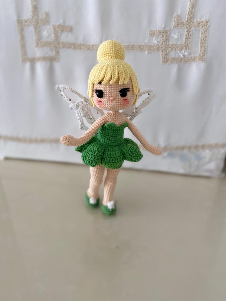 May include: A crocheted fairy doll with blonde hair, a green dress, and white wings. The doll has a sweet, cartoon-like face.