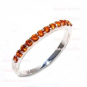 May include: A silver ring with a band of small, round, orange gemstones. The ring is set against a white background. The text "Heaven Jewelry" is visible in the background.
