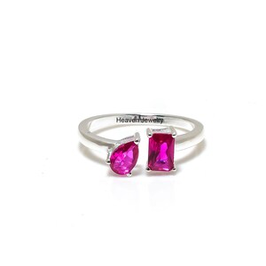 Peut inclure: Bague en argent ornée de deux pierres roses vives, une en forme de poire et une rectangulaire. La bague est présentée sur fond blanc, avec le texte "Heaven Jewelry" gravé sur le corps.