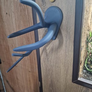 Puede incluir: Un perchero de pared de pl&aacute;stico gris en forma de cuerno de ciervo con tres ganchos. El perchero est&aacute; montado en una superficie de imitaci&oacute;n de madera.