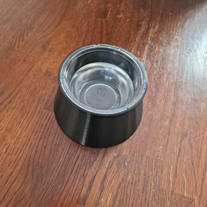 May include: A black plastic pet bowl with a clear plastic insert. The bowl has a raised lip around the edge and a textured bottom.