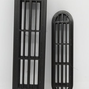 May include: Two black, arched-top vent covers. The larger one is approximately 20 cm long, with a series of vertical bars and a decorative border. The smaller vent cover mirrors the design, about 10 cm in length. Both are set against a white background.