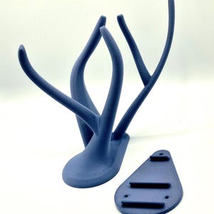 May include: A blue 3D printed deer antler wall mount with a separate base. The antlers are curved and have a smooth finish. The base is a flat, triangular shape with three holes for mounting.