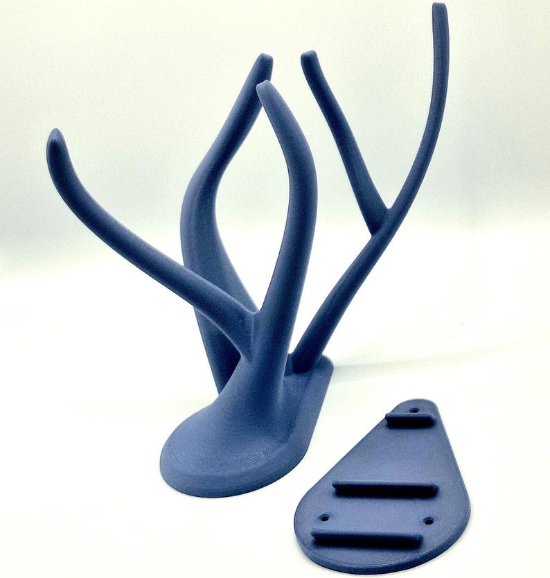 Puede incluir: Un soporte de pared de asta de ciervo impreso en 3D azul con una base separada. Las astas son curvadas y tienen un acabado liso. La base es de forma triangular plana con tres agujeros para montaje.