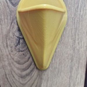 May include: A yellow plastic wall-mounted holder with a triangular shape and a rounded top.