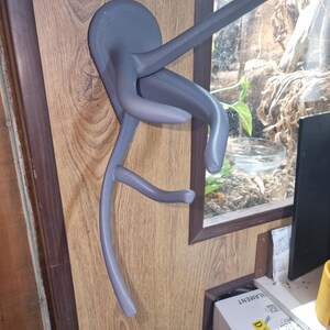 Puede incluir: Un soporte de pared gris impreso en 3D para colgar una guitarra. El soporte tiene forma de rama de &aacute;rbol estilizada con una base circular.