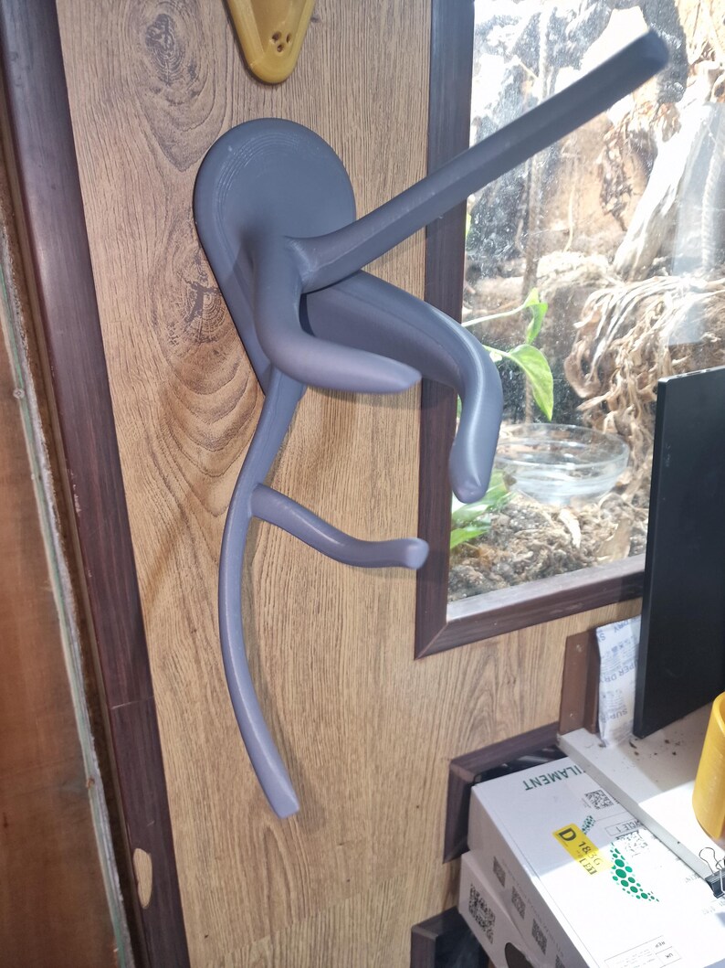 Puede incluir: Un soporte de pared gris impreso en 3D para colgar una guitarra. El soporte tiene forma de rama de &aacute;rbol estilizada con una base circular.