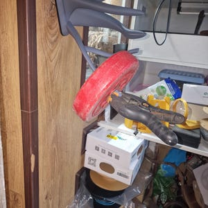 Puede incluir: Un gancho de pared en forma de pulpo de color gris impreso en 3D con cinco brazos. Una placa de peso roja est&aacute; colgando de uno de los brazos. Una abrazadera negra mantiene la placa de peso en su lugar.