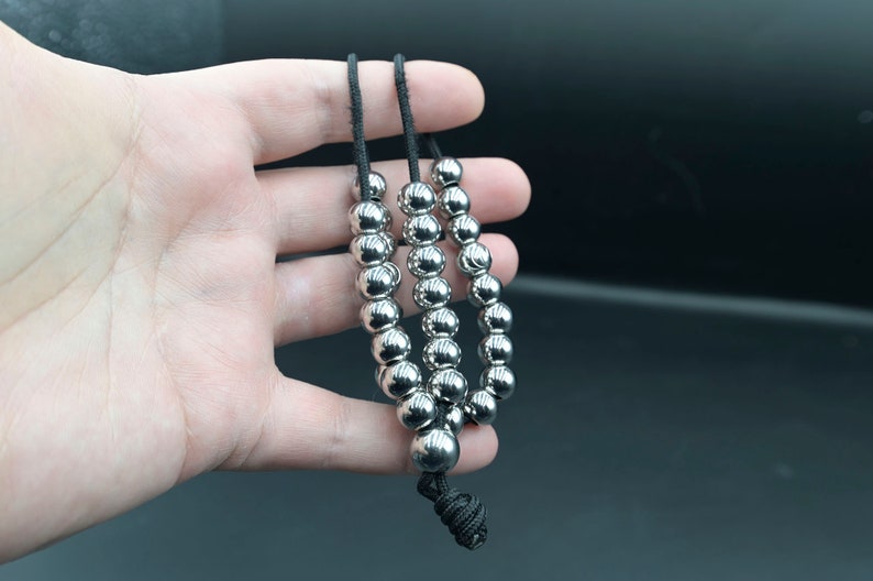 May include: A silver beaded necklace with three strands of beads. The beads are round and smooth, and the necklace is strung on a black cord.