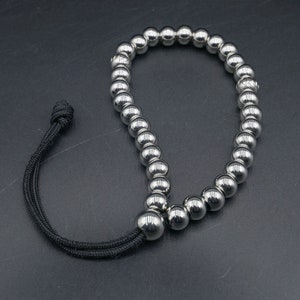 May include: A silver beaded bracelet with a black cord and adjustable clasp. The bracelet is made of small, round beads that are strung together on a cord.