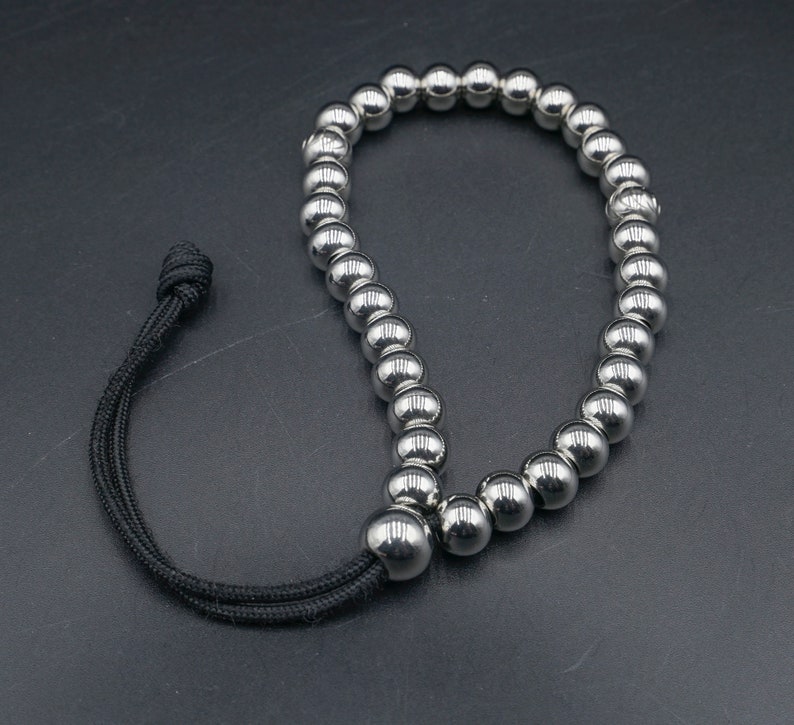 May include: A silver beaded bracelet with a black cord and adjustable clasp. The bracelet is made of small, round beads that are strung together on a cord.