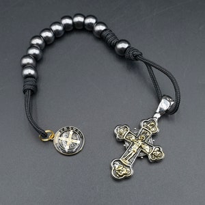 May include: A black beaded rosary with a silver and gold cross pendant. The cross features a detailed design with a figure of Jesus Christ.