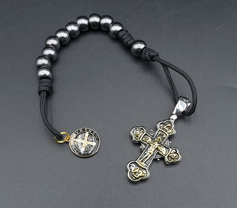 May include: A black beaded rosary with a silver and gold cross pendant. The cross features a detailed design with a figure of Jesus Christ.
