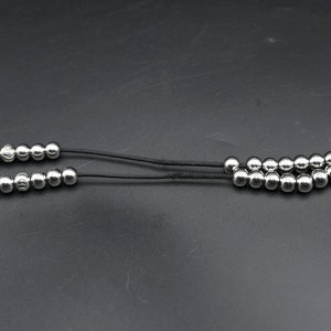 May include: A silver beaded necklace with a black cord. The necklace has a total of 18 beads.