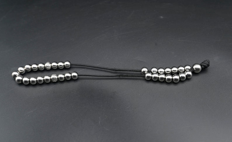 May include: A silver beaded necklace with a black cord. The necklace has a total of 18 beads.