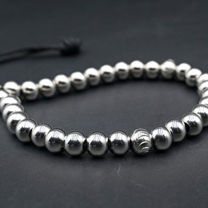 May include: A silver beaded bracelet with a black cord closure. The beads are round and have a polished finish.