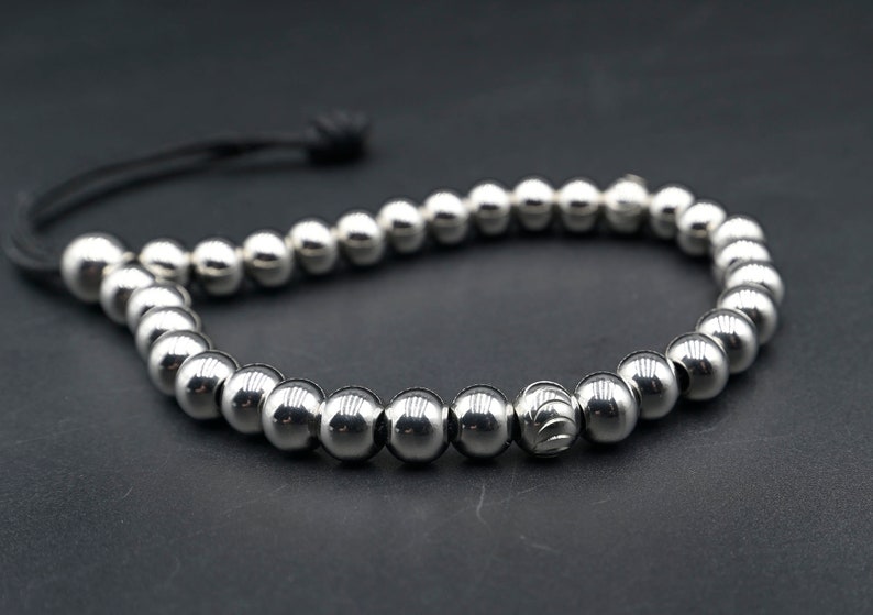 May include: A silver beaded bracelet with a black cord closure. The beads are round and have a polished finish.