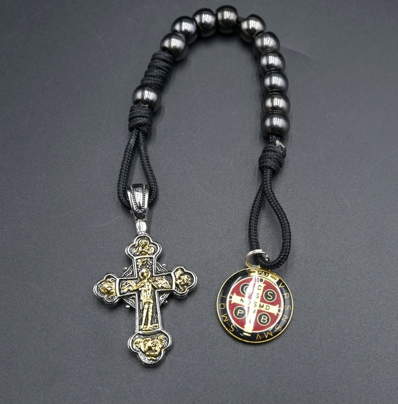 May include: A black cord rosary with a silver and gold cross pendant and a round silver and red medal pendant. The medal has the inscription "S.S.M.D. P.B. A.W.S.V.R.S."