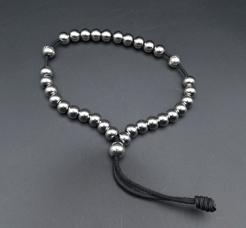 May include: A silver beaded bracelet with a black cord and a knot at the end.
