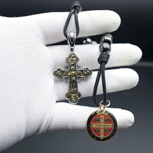 May include: A black cord necklace with a silver and gold cross pendant and a round, red, black, and gold medal pendant. The medal has the words "S.P.Q.R." and "O.W.S.S.N.S." around the edge.