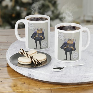 Może przedstawiać: Dwa białe ceramiczne kubki z kreskówkową ilustracją osoby z dymkiem, w którym napisano "Natalie i kawa dla sztuki..." Osoba wskazuje na mniejszy dymek, w którym napisano "To się nazywa malowanie".