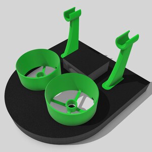 May include: A green 3D printed drone stand with two circular landing pads and two vertical supports. The stand is designed to hold a drone securely during storage or transport.