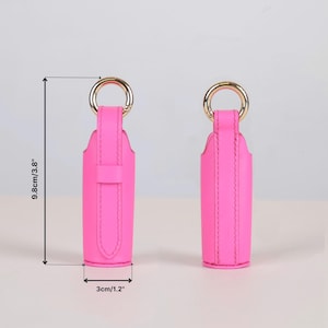 May include: Two bright pink lipstick cases with gold-tone metal rings at the top. The cases feature a vertical strap design and measure 3.8 inches in height and 1.2 inches in width as indicated by the visible measurement lines and text.